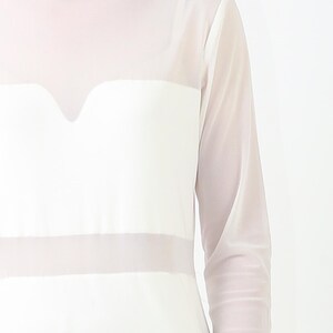 May include: A white long-sleeved top featuring a mock neck and a sheer mesh overlay. The garment includes a solid opaque panel across the chest with a sweetheart-shaped neckline detail and a horizontal sheer band across the midsection.