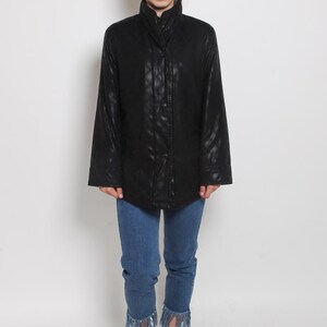 May include: A black quilted jacket with a high collar and a zipper closure. The jacket has a slightly fitted silhouette and is worn with blue jeans and black sneakers.