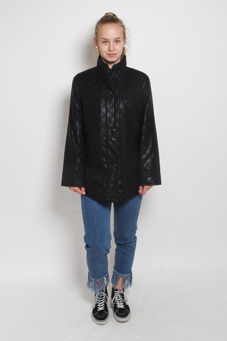 May include: A black quilted jacket with a high collar and a zipper closure. The jacket has a slightly fitted silhouette and is worn with blue jeans and black sneakers.