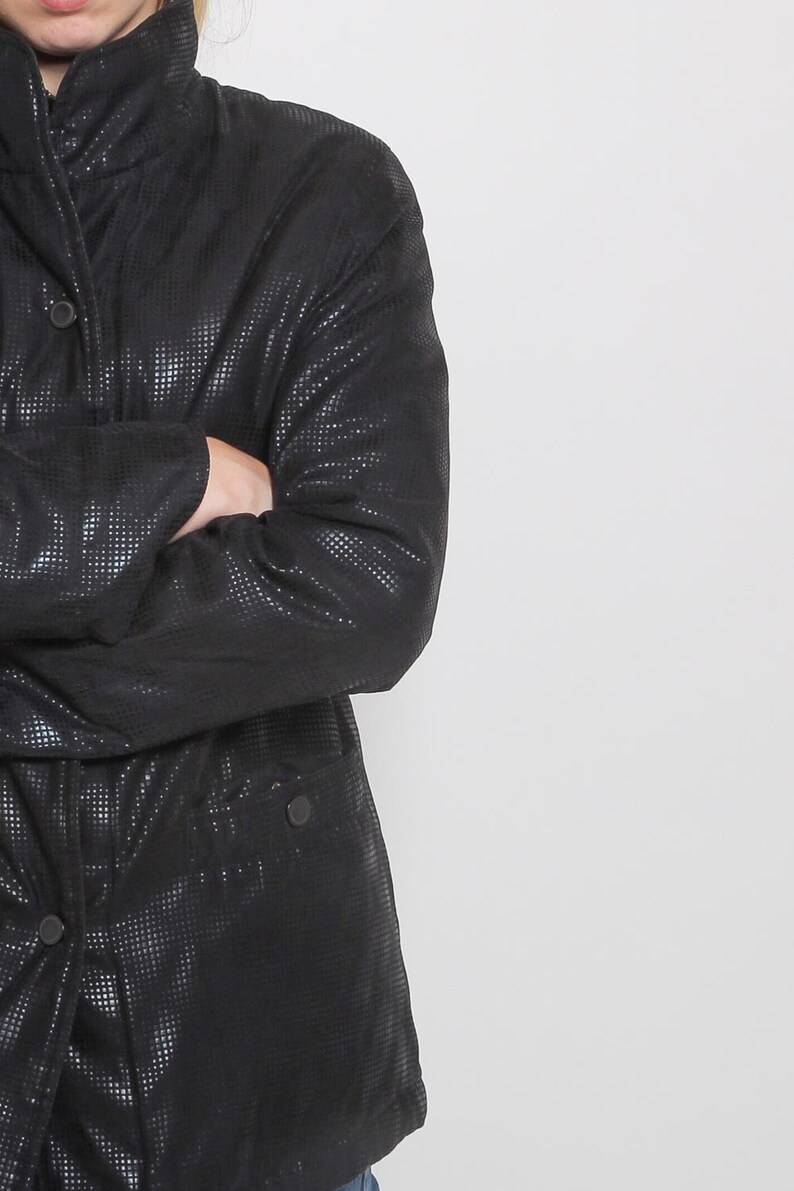 May include: A black quilted jacket with a high collar and a button closure. The jacket has a textured, almost sparkly, finish.
