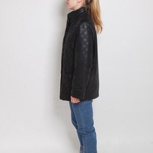 May include: A black quilted jacket with a zipper closure and a stand-up collar. The jacket is worn by a person wearing blue jeans and black high-top sneakers.