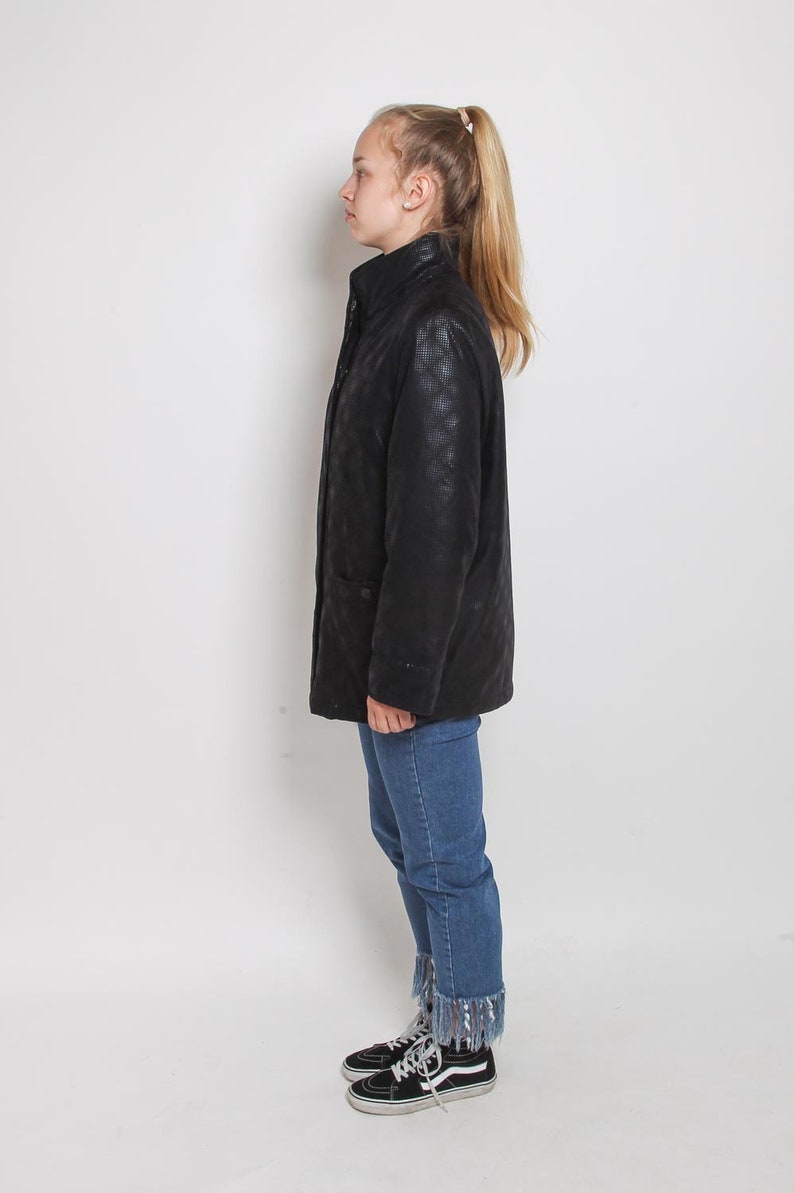 May include: A black quilted jacket with a zipper closure and a stand-up collar. The jacket is worn by a person wearing blue jeans and black high-top sneakers.