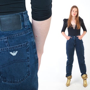 May include: A pair of dark blue denim jeans with a back pocket featuring a white embroidered logo. The jeans have a high waist and a straight leg.