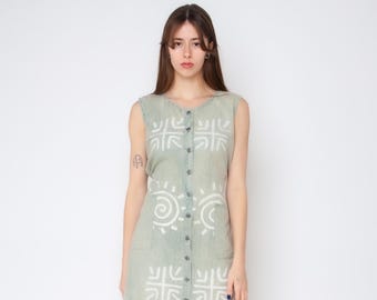 May include: A sleeveless, sage green midi dress featuring a front button-down closure and a white printed pattern consisting of repeating geometric cross shapes and circular sun-like motifs distributed across the front of the garment.
