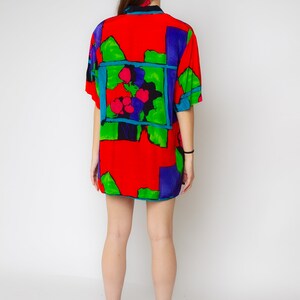 Pode incluir: Uma camisa de manga curta vermelha, verde, azul e roxa com uma estampa floral abstrata.