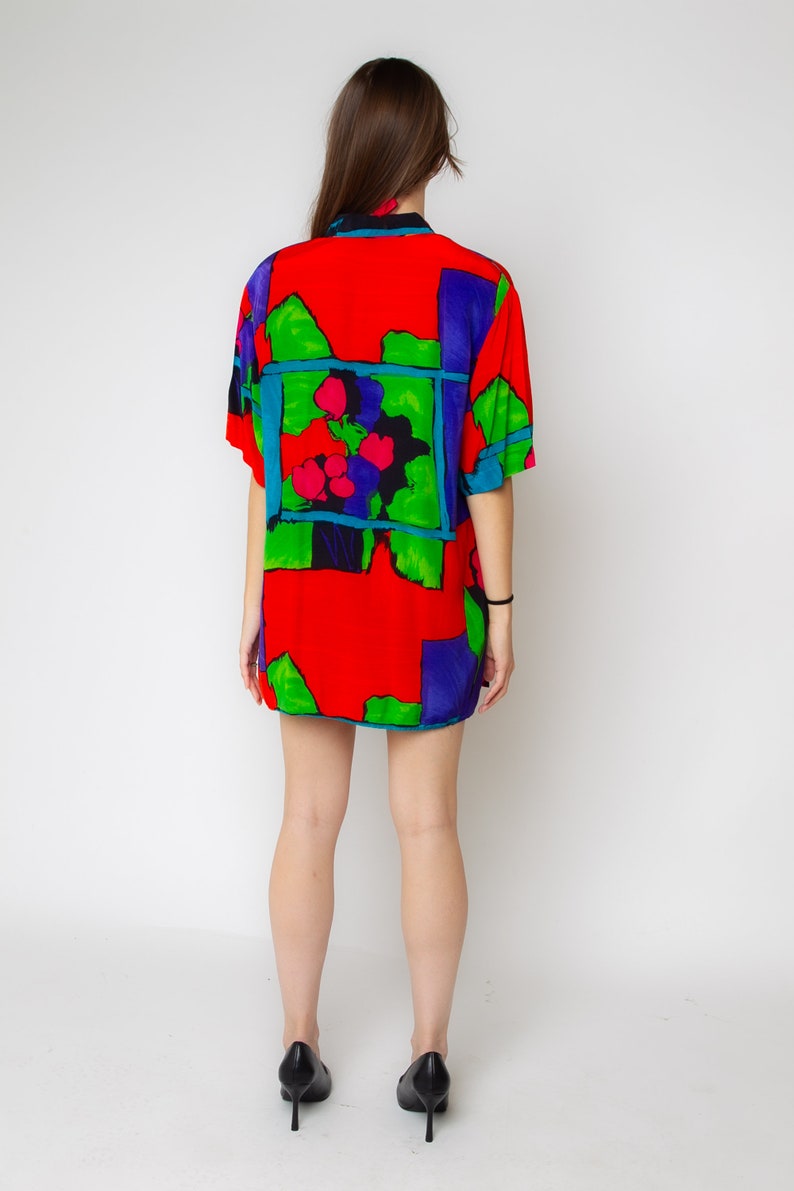 Pode incluir: Uma camisa de manga curta vermelha, verde, azul e roxa com uma estampa floral abstrata.