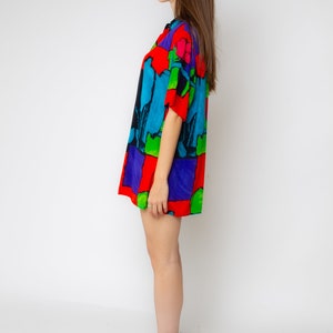 Pode incluir: Uma mulher vestindo um vestido de camisa de manga curta com estampa abstrata colorida e saltos altos pretos.