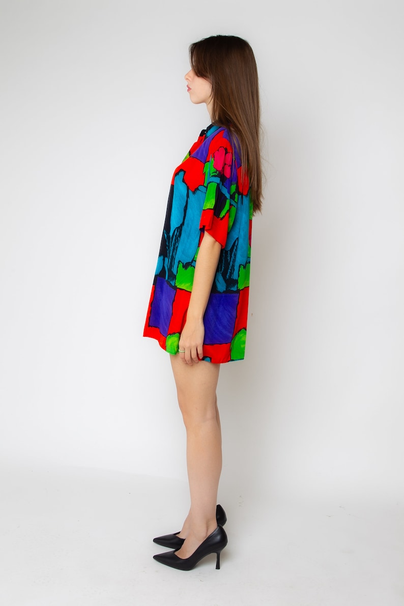 Pode incluir: Uma mulher vestindo um vestido de camisa de manga curta com estampa abstrata colorida e saltos altos pretos.