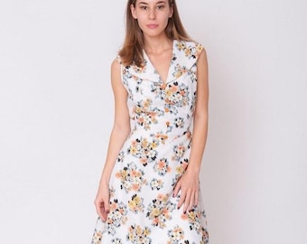 May include: A sleeveless white dress featuring a repeating floral pattern in shades of orange, yellow, and grey. The dress has a wide, pointed collar, a fitted bodice, and a flared skirt that falls to the knee, creating a structured silhouette.