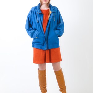 May include: A woman wearing a blue jacket over a rust-coloured dress and brown knee-high boots.