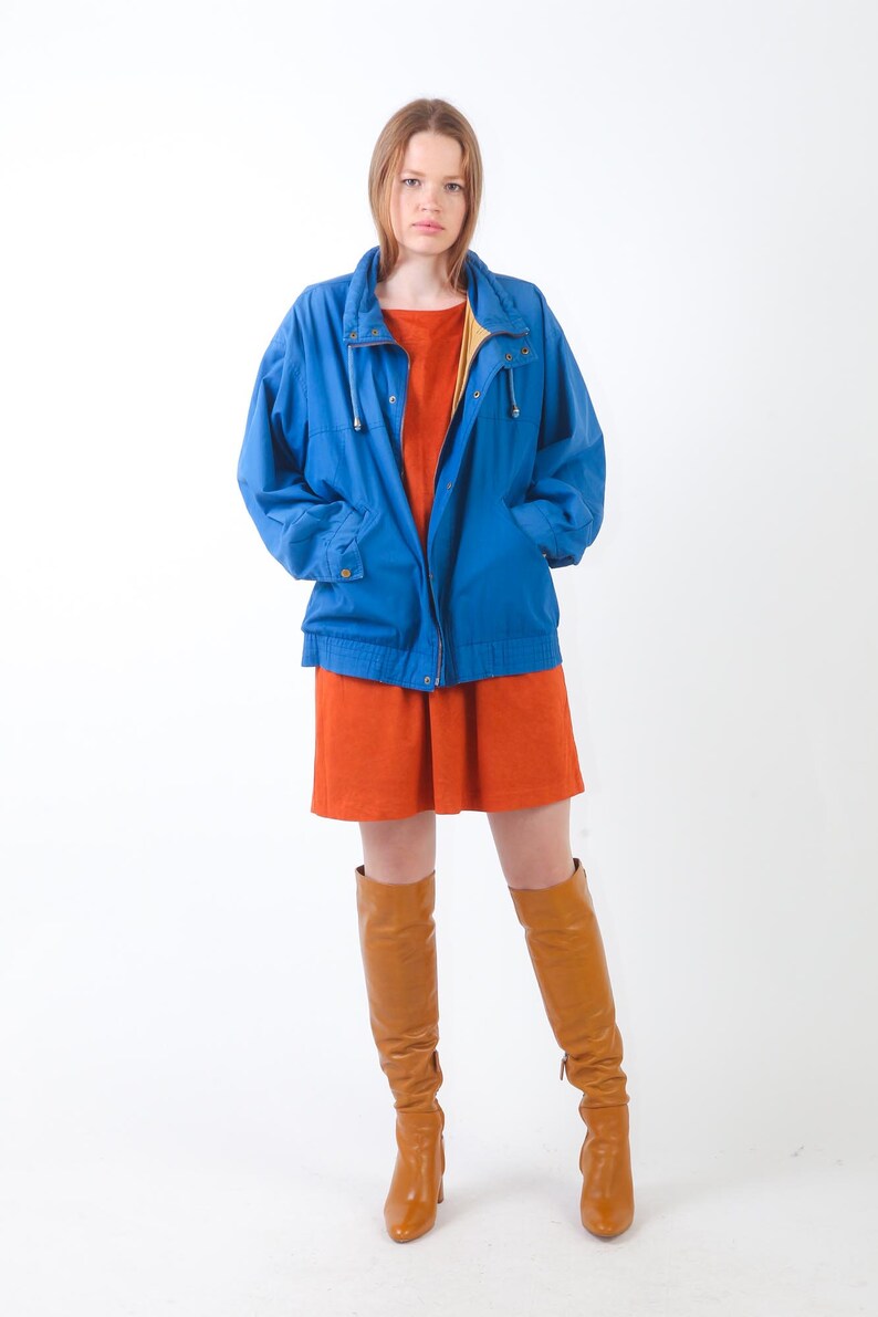 May include: A woman wearing a blue jacket over a rust-coloured dress and brown knee-high boots.