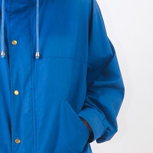 May include: A blue jacket with a drawstring hood and a zip closure. The jacket has a pocket on the left side and a button fastening.