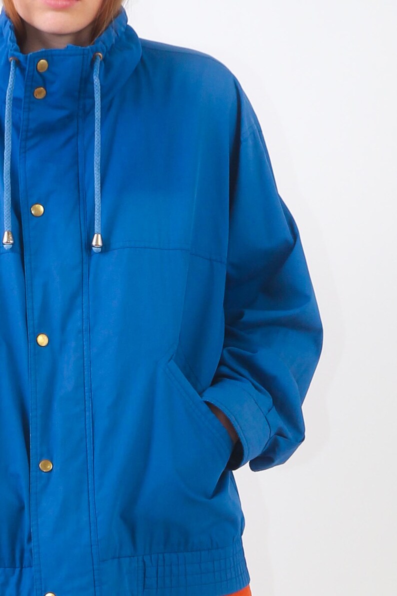May include: A blue jacket with a drawstring hood and a zip closure. The jacket has a pocket on the left side and a button fastening.