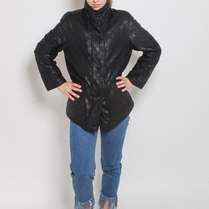 May include: A black quilted jacket with a zipper closure and a buttoned flap. The jacket has a stand-up collar and is worn over blue jeans with frayed hems. The person is wearing black high-top sneakers.