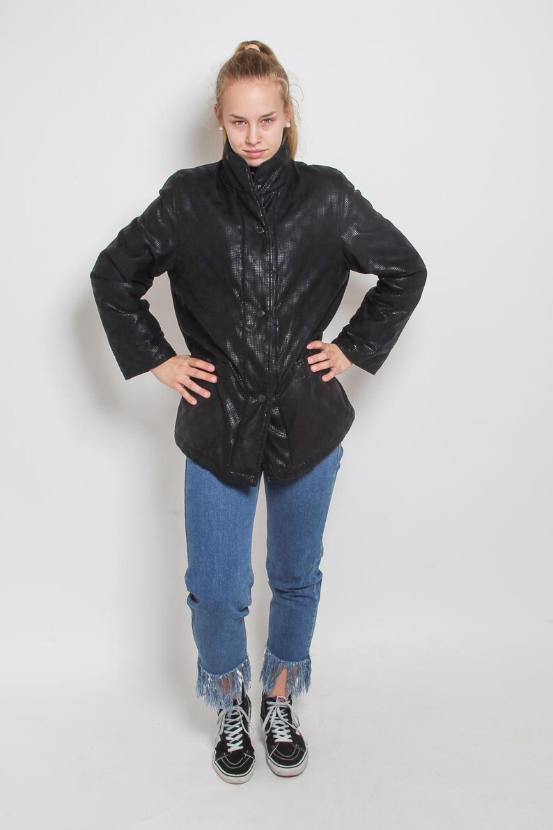 May include: A black quilted jacket with a zipper closure and a buttoned flap. The jacket has a stand-up collar and is worn over blue jeans with frayed hems. The person is wearing black high-top sneakers.