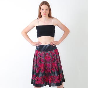 May include: A black tube top with thin straps paired with a knee-length skirt featuring a dark background and a vibrant floral pattern in shades of red, pink, and green. The skirt has a wide, solid black waistband and a flared, pleated silhouette.