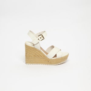 May include: White wedge sandals with a buckle closure and a woven platform sole.