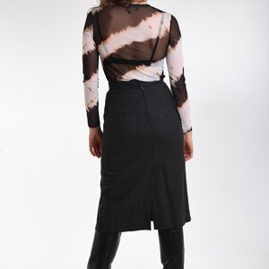 May include: A long-sleeve mesh top featuring a black and white diagonal tie-dye pattern, worn over a black undergarment. Paired with a charcoal gray midi-length skirt that has a center back zipper and a vertical slit, and black knee-high boots.