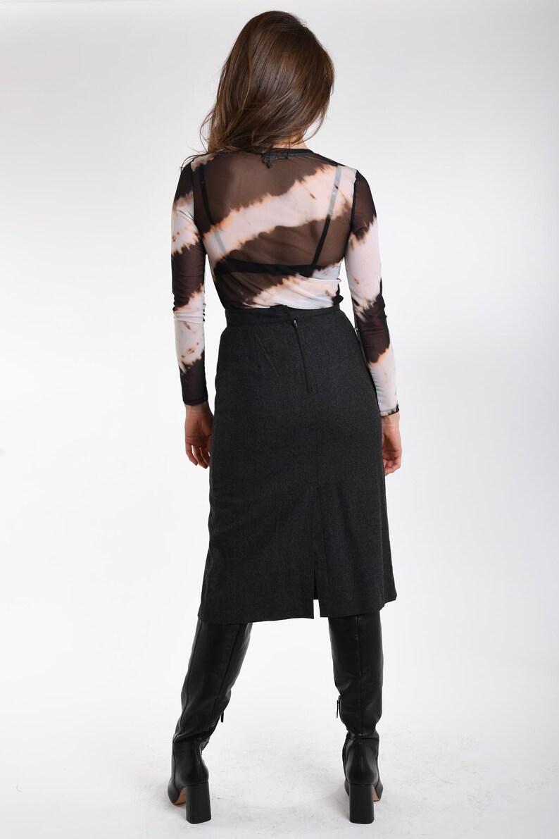 May include: A long-sleeve mesh top featuring a black and white diagonal tie-dye pattern, worn over a black undergarment. Paired with a charcoal gray midi-length skirt that has a center back zipper and a vertical slit, and black knee-high boots.