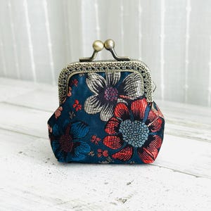 May include: A small, floral coin purse with a metal clasp. The purse features a dark blue background with large, colorful flower designs in red, silver, and blue. The clasp is a bronze color.