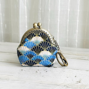May include: A small, vintage-style coin purse with a brass clasp and chain. The purse features a fan-shaped pattern in shades of blue, white, and navy. The purse is likely used for carrying coins, small items, or as a decorative accessory.