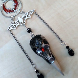 May include: A silver pendant with a bat design, a red moon, and a long, pointed, gray and white crystal. The crystal is adorned with silver gears and a red jewel. The pendant hangs from a silver chain with three black beads.