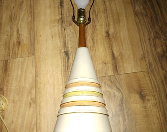 May include: A white ceramic table lamp with a brown wooden base and a brown base. The lamp has a white shade with yellow and orange stripes.