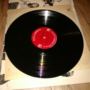 May include: A black vinyl record with a red Columbia Records label. The label has the text "Columbia" and "Stereo" printed on it. The record is on a white surface.