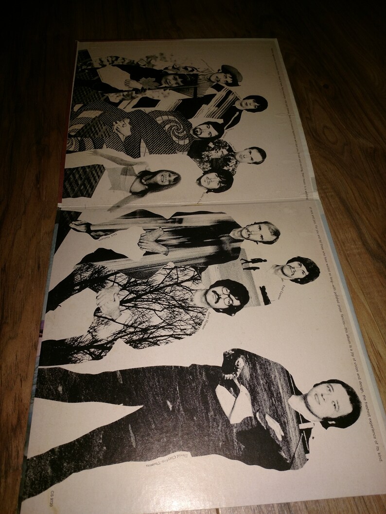 May include: A black and white photo of a band, the members are standing in a row, some are looking at the camera, others are looking away. The photo is on a white background with the band's name printed at the bottom.