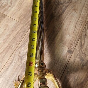 May include: A vintage brass lamp base, approximately 22 inches tall, with a fluted column and ornate base. The lamp has a decorative shell-like element near the top and a three-footed base. The lamp is unlit and has a cord.