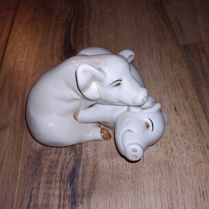 May include: A pair of white ceramic pig salt and pepper shakers. The pigs are positioned as if one is cuddling the other.
