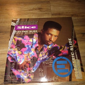 May include: A vinyl record cover featuring Grandmaster Slice with the title "Electric Slide (Shall We Dance)". The cover is a vibrant blue, purple, and yellow color scheme with a circuit board design. The artist is wearing a colorful shirt and has a serious expression.