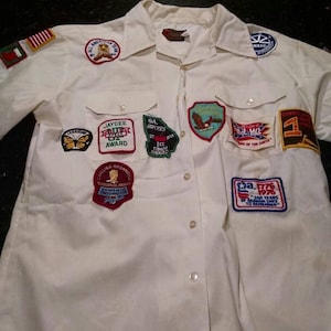 May include: White long-sleeve button-down shirt with various embroidered patches, including a Jaycee Outstanding Young Man Award, a Georgia Jaycees 1st Dime Award, and a Georgia 1776 Bicentennial patch.