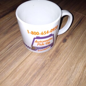 May include: White ceramic mug with a curved handle. The mug features the text "1-800-654-0920" in orange, and a purple and orange graphic that reads "Automatic Pick-Up" and "Federal Express".