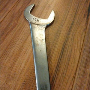 May include: A silver wrench with a 1 7/8 inch opening. The wrench is on a wooden surface.