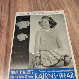 May include: A vintage knitting pattern booklet for lumber jackets for children. The cover features a young girl wearing a pink knitted lumber jacket with a floral skirt. The booklet is titled "Bairnswear 1388 Lumber Jackets for the First 5 Years".