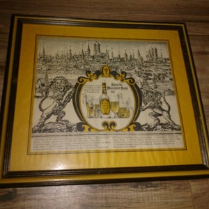 May include: A framed vintage advertisement for a German beer called "Münchner Hell" featuring a cityscape, two lions, and a bottle of beer.