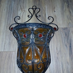 May include: A decorative wall sconce with a wrought iron frame and amber glass. The sconce has a traditional design with intricate details and red glass accents.
