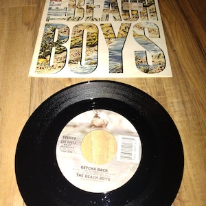 May include: A black vinyl record with a white label. The label has the text "Stereo ZS4 04913 AA-AF 284 04913-3 Time: 2:59 Getcha Back (Live) - Merten Taken from The Carousel THE BEACH BOYS B2 THE BEACH BOYS Produced by Mike Love" printed on it.