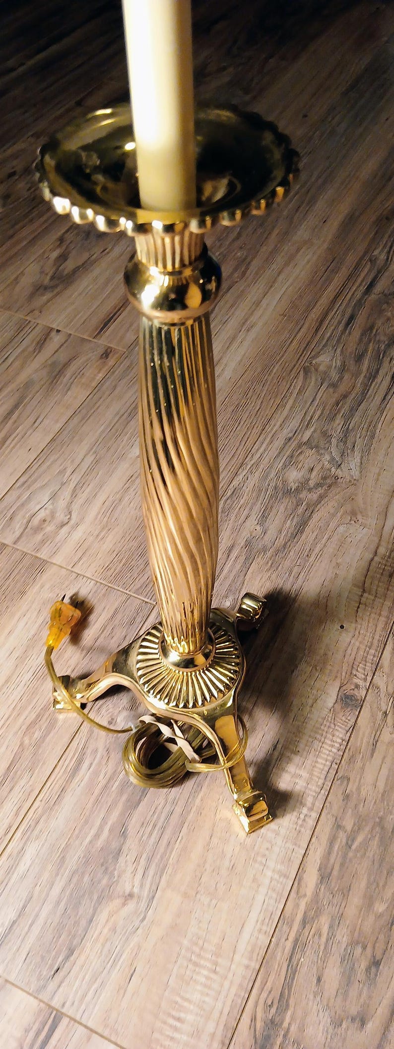 May include: A gold-colored electric candle lamp with a fluted column and a scalloped candle holder. The base has a decorative design and three feet. A cream-colored candle is in the holder.