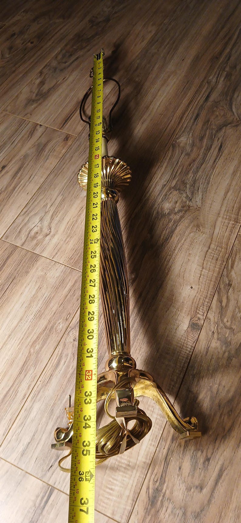 May include: A gold-colored lamp base with a fluted column design, measuring approximately 37 inches in height. The base has a decorative, ornate design and is shown with a measuring tape.