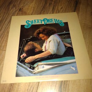 May include: A vintage vinyl record album cover featuring a couple in a convertible car. The album cover is yellow with the title "Sweet Dreams" in a stylized font and the text "The Life and Times of the  Dream  Band" in a smaller font. The couple is embracing and smiling at each other. The album cover is in good condition with some minor wear and tear.
