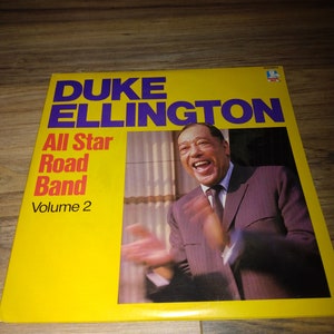 May include: A yellow vinyl record album cover featuring a photo of Duke Ellington, a famous jazz musician, smiling and clapping. The album title is "Duke Ellington All Star Road Band Volume 2".