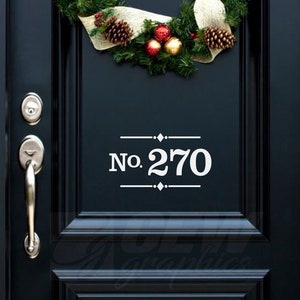 May include: A black front door with a Christmas wreath and the house number 270 in white. The wreath is decorated with pine cones, red and gold ornaments, and greenery. The door has a silver handle and a glass panel.