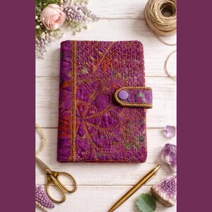 May include: A rectangular journal cover in a vibrant purple fabric featuring intricate gold-toned quilted stitching in a floral pattern. The cover includes a matching purple fabric strap with a single purple snap button closure on the right side.