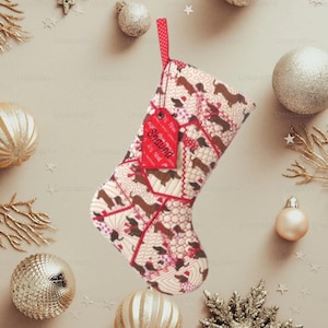 May include: A quilted Christmas stocking featuring a repeating pattern of brown dachshunds wearing Santa hats on a cream background. The stocking has red trim, a red hanging loop, and a red tag with the name Shauna printed in black text.