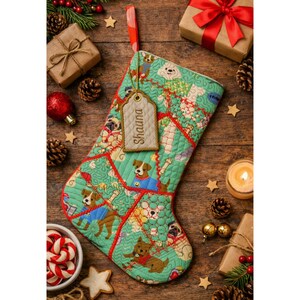 May include: A quilted Christmas stocking in a light green fabric featuring a repeating pattern of various dog breeds wearing sweaters. A beige fabric tag attached to the top loop displays the embroidered name Shauna in brown thread.