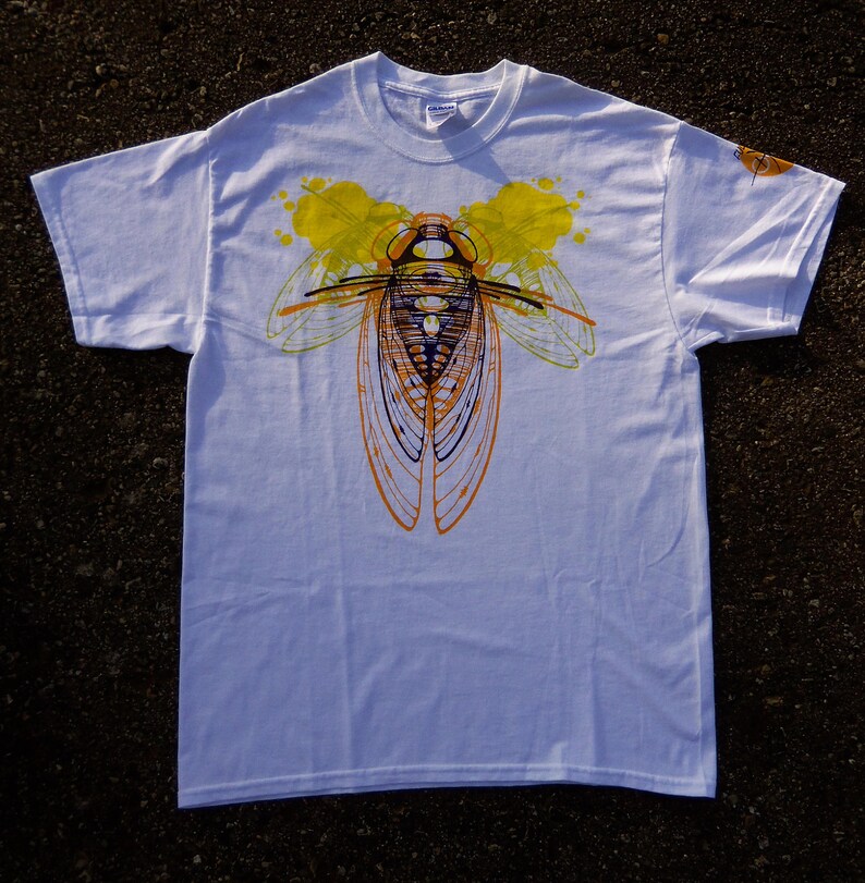 Pode incluir: Camiseta branca com uma estampa gr&aacute;fica de uma cigarra em amarelo, laranja e preto. A cigarra &eacute; contornada em preto e tem um corpo roxo.