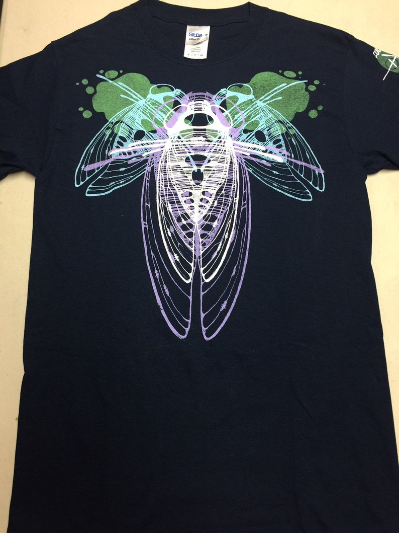 Pode incluir: Uma camiseta azul escura com um gr&aacute;fico branco de uma cigarra com detalhes verdes e roxos.
