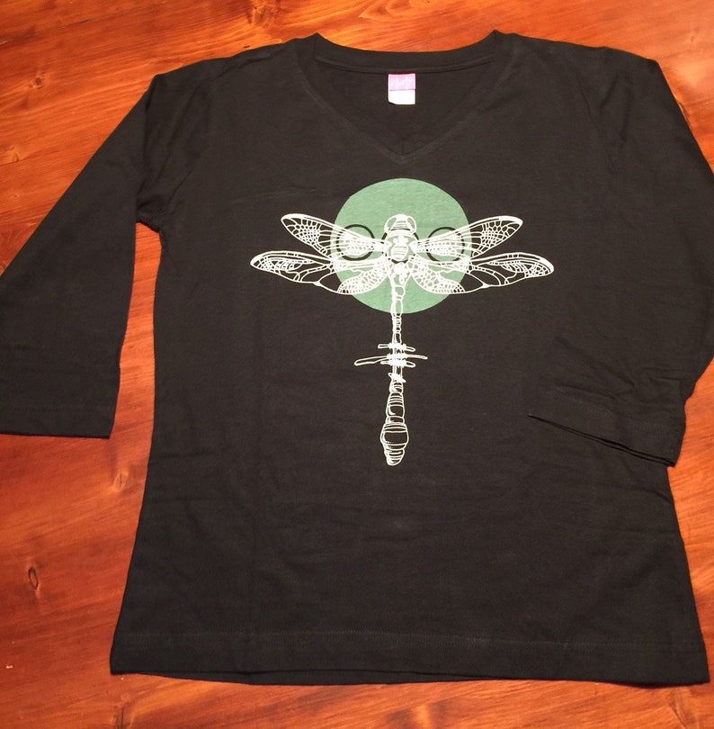 May include: Black long-sleeve shirt with a white dragonfly graphic and a green circle behind it.